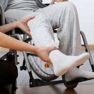An image of a person in a wheelchair with another person examining their lower limb.