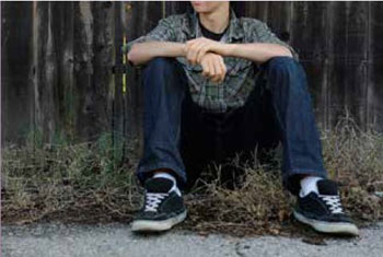 Photo of a teenager seated on the ground, with their face out of frame
