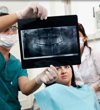 Photo of a dentist, technician and patient examining a dental x-ray