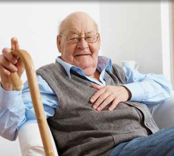 Photo of a male senior citizen, smiling, seated and holding a walking stick.