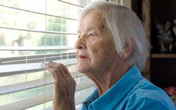 Photo of a female senior citizen looking out a window through venetian blinds